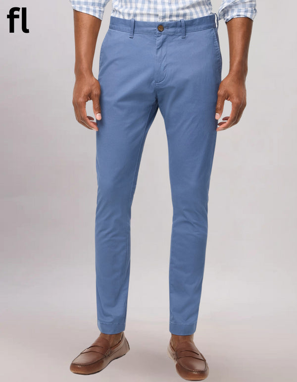 A man wearing a checkered shirt and blue chinos standing against a white background.